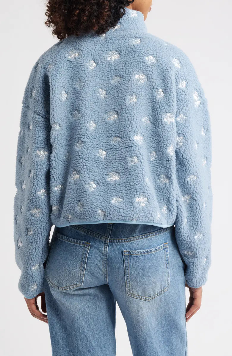 Person wearing a blue fleece jacket with white floral patterns on a plain background