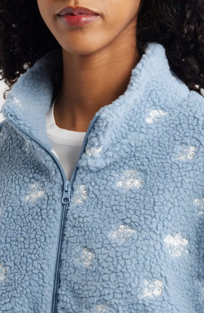 Close-up of a person wearing a light blue fleece jacket with embroidered floral pattern.